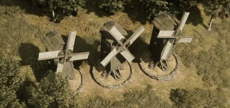 Trois moulins à vent tournant côte à côte au bord d’un bois, vus du ciel
